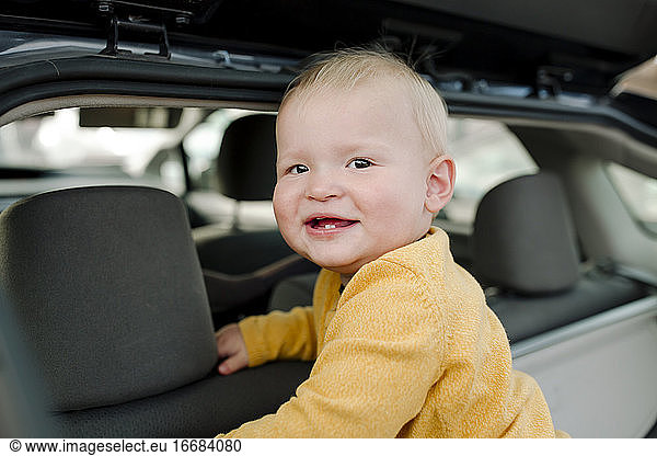 Glückliches Baby mit ersten Zähnen und gelbem Hemd in einem offenen Geländewagen