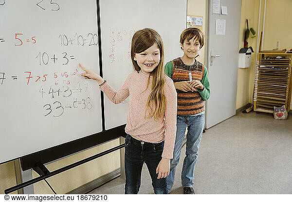 Glückliches Mädchen  das mit einem Jungen im Klassenzimmer ein mathematisches Problem löst