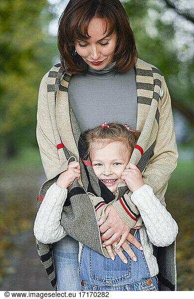 Glückliches Mädchen versteckt sich in Mutters Strickjacke im Park