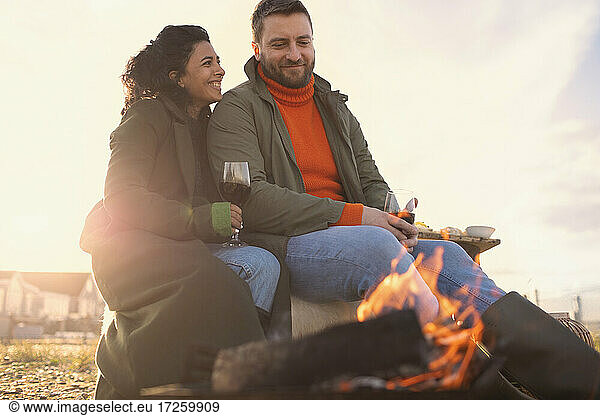 Glückliches Paar genießt Rotwein am Feuer am Winterstrand