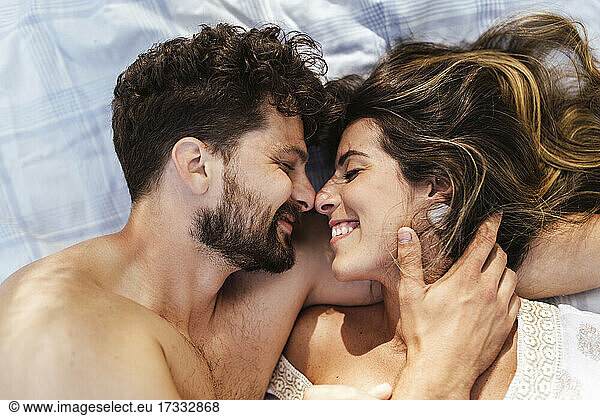 Glückliches Paar mit geschlossenen Augen  das sich gegenseitig auf einer Picknickdecke umarmt