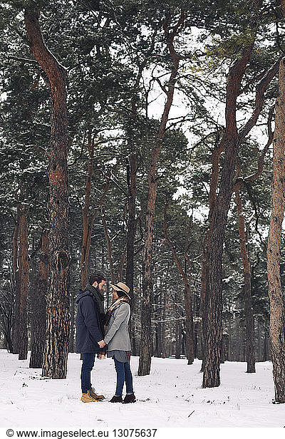 Glückliches Paar sieht sich an  während es auf einem schneebedeckten Feld im Wald steht