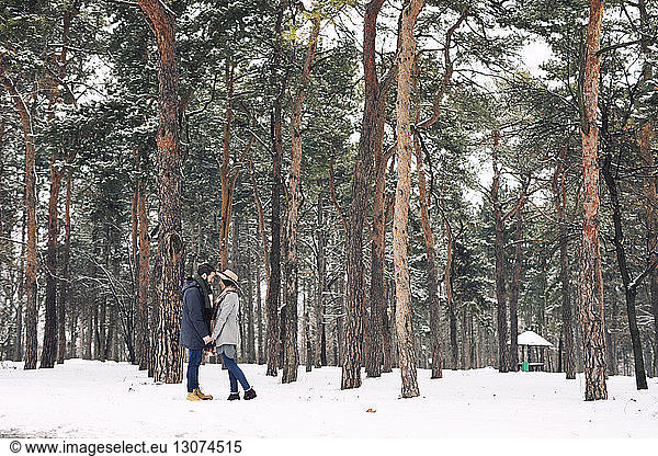 Glückliches Paar sieht sich an  während es auf einem verschneiten Feld im Wald steht