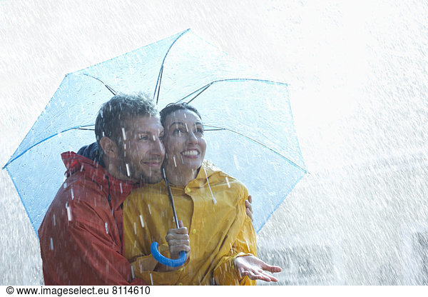 Glückliches Paar unter Schirm im Regen