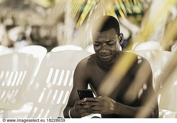Glad black man using smartphone on beach