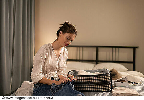 Glad woman packing clothes on bed