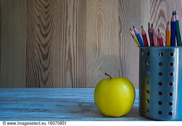 Glas mit Buntstiften und einem Apfel.