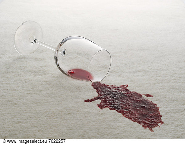 Glas Rotwein auf weißem Teppich verschüttet