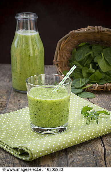 Glass bottle and glass of green smoothie  made of spinach  rocket salad  apple  orange  banana and cucumber  on cloth wooden table