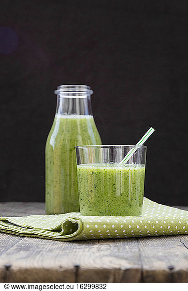 Glass bottle and glass of green smoothie  made of spinach  rocket salad  apple  orange  banana and cucumber  on wooden table