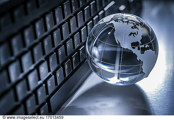 Glass globe and computer keyboard on gray background