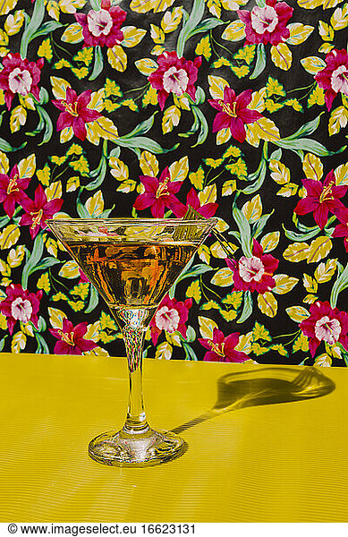 Glass of Cocktail liquor kept on yellow table against flower background