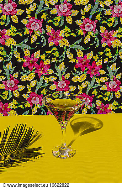 Glass of Cocktail liquor kept on yellow table with palm leaf in studio