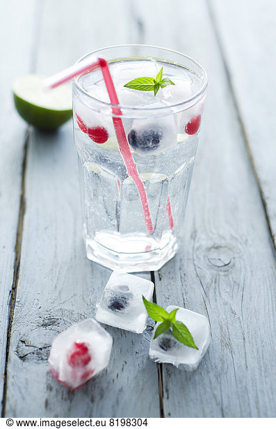 Glass of mineral water with ice cubes and frozen berries on wooden table  close up