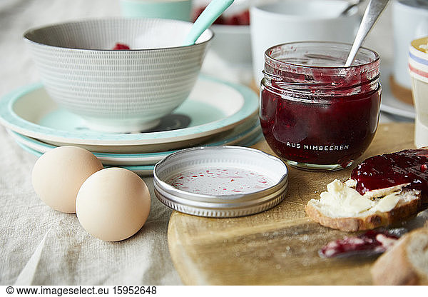 Glass of raspberry jam  bread with jam and two eggs on breakfast table