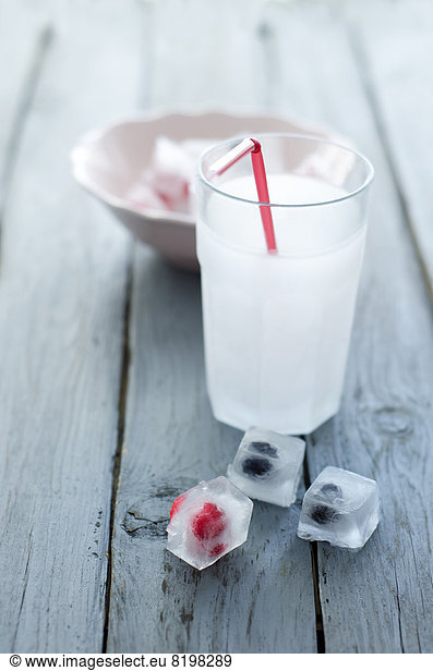 Glass of soda with ice cubes and frozen berries on wooden table  close up