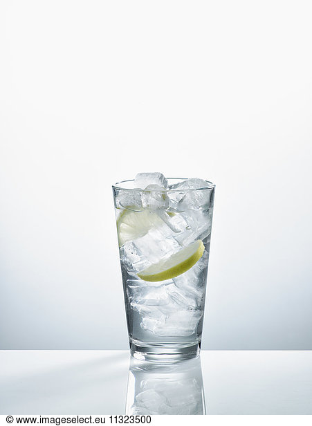 Glass with mineral water  ice cubes and slices of lemon in front of white background