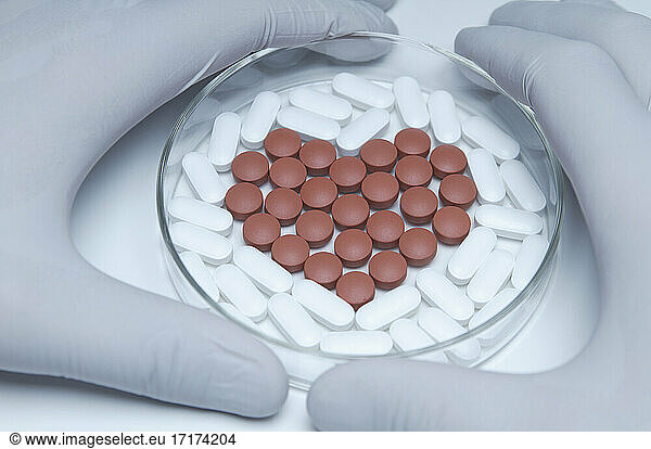 Gloved hands holding a petri dish with generic pills forming heart symbol
