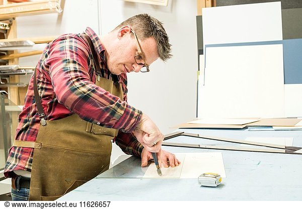 Goirle  Netherlands. Mid adult male craftsman and picture framemaker  cutting up sheets of glass for a new picture frame.
