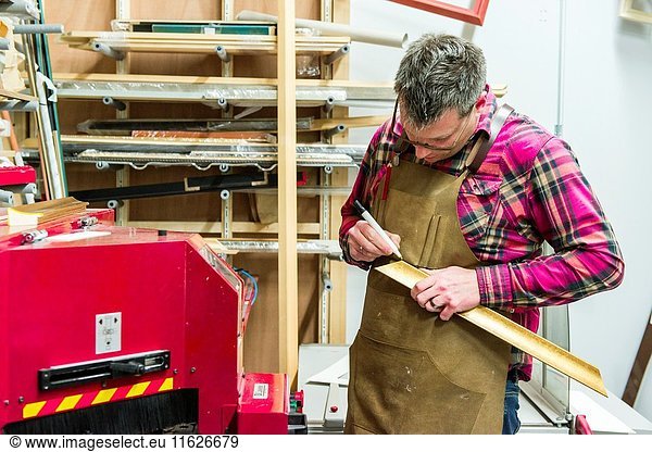 Goirle  Netherlands. Mid adult male craftsman and picture framemaker working on an assignment for a custiomer inside his workshop.