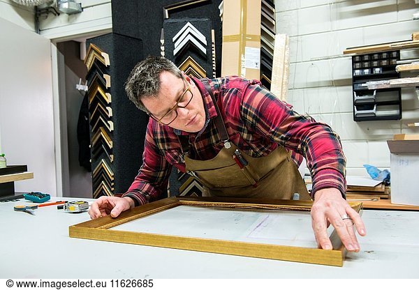 Goirle  Netherlands. Mid adult male craftsman and picture framemaker working on an assignment for a custiomer inside his workshop.