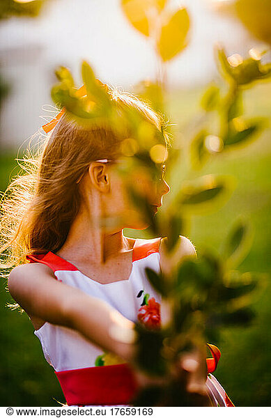 Golden light on blond girl with green foliage and bush