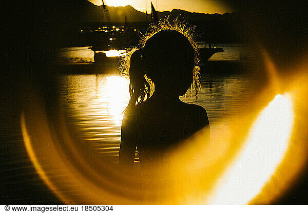 Golden light silhouette of young girl next to water and boats