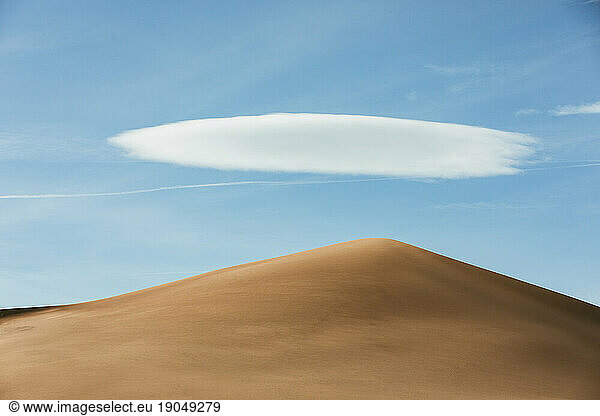 golden tan sand dune under blue sky with one puffy white cloud
