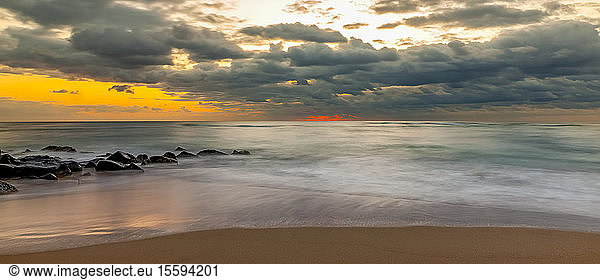 Goldener Sonnenuntergang über dem Meer mit dunklen Wolken und Brandung  die an den Strand gespült wird; Kauai  Hawaii  USA