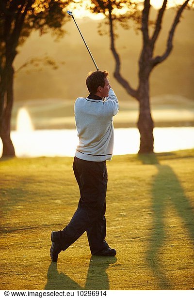 Golfer im Sonnenlicht  der einen Golfschläger hält  der einen Golfschwung nimmt und wegschaut.