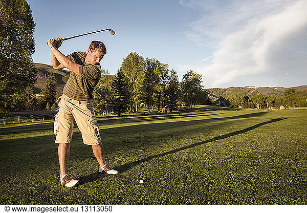 Golfer swinging golf club while standing on grassy field