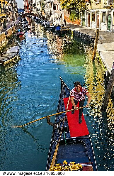 Gondel und Gondoliere in bunten kleinen Kanal schafft schöne Reflexionen in Venedig Italien.