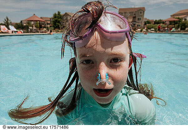 Goofy young girl in pool with goggles on forehead