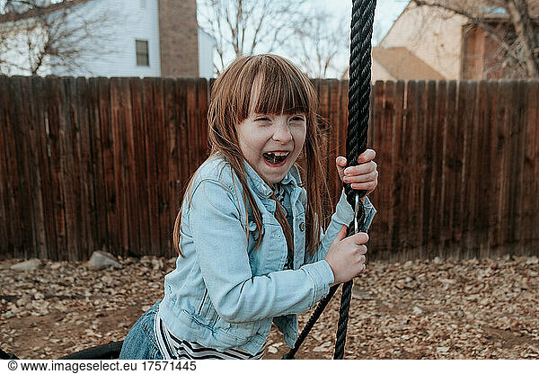 Goofy young girl playing on swing in backyard