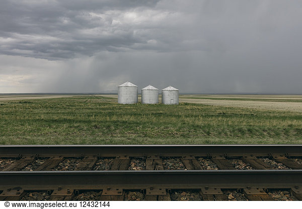 Grain silos and storm clouds over vast areas of farmland and prairie  train tracks in foreground