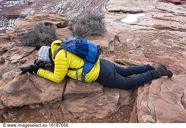 Grand View Point  Tourist lies on the ground for photography  rocky ground  Monument Basin  White Rim  Island in the Sky  Canyonlands National Park  Utah  USA  North America