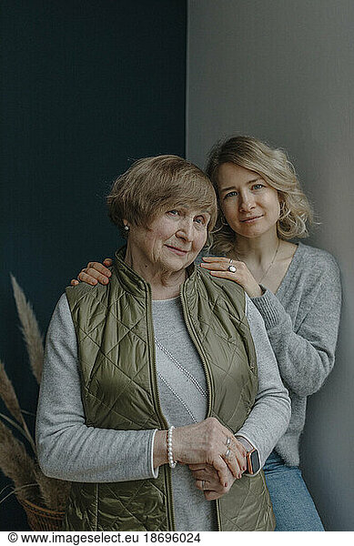Granddaughter leaning on wall with grandmother at home