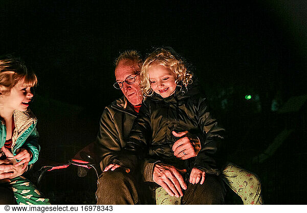 Granddaughter sitting on Grandfathers lap sitting around fire pit