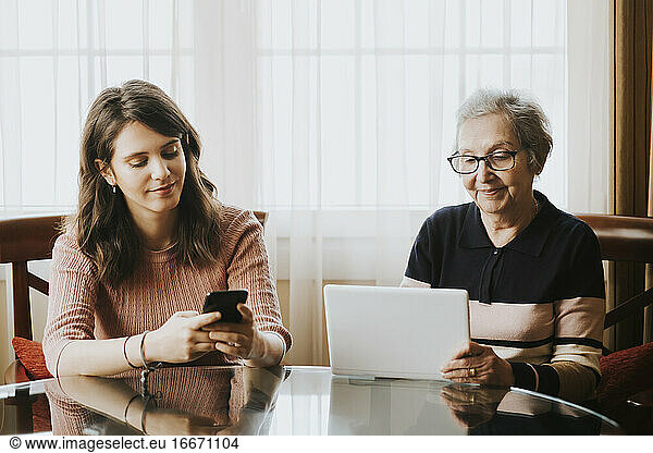granddaughter using mobile and grandmother using tablet