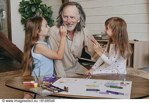 Granddaughters having fun painting grandfather's face at home