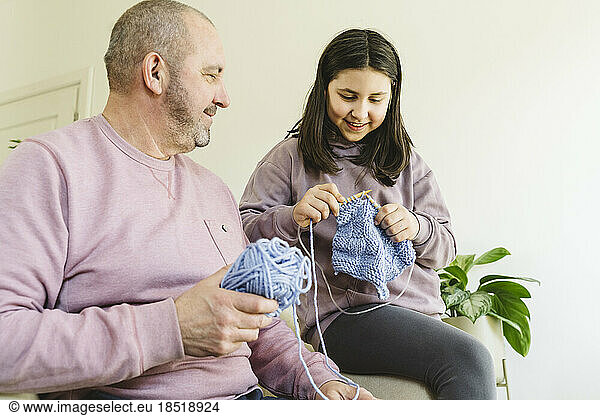 Grandfather and granddaughter knitting sweater at home