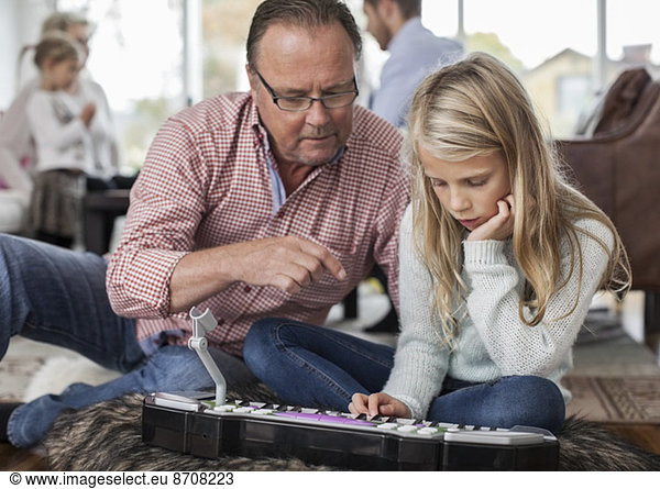 Grandfather and granddaughter playing piano with family in background at home