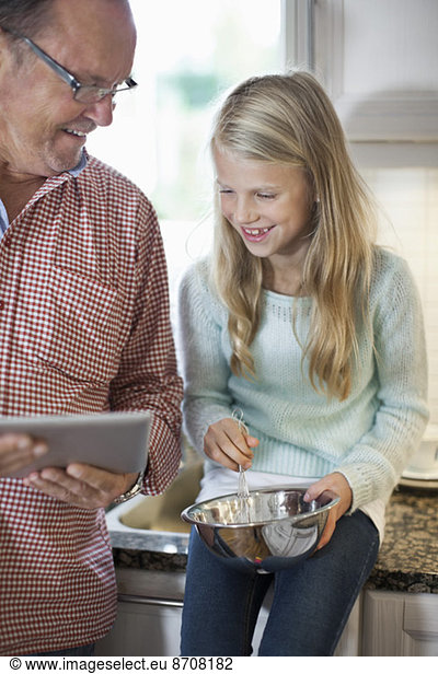 Grandfather and granddaughter using digital tablet while cooking in kitchen