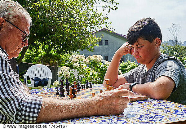 Grandfather and grandson playing chess in the garden