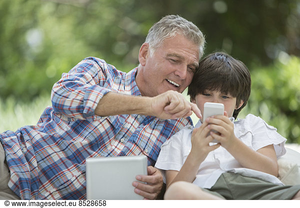 Grandfather and grandson using digital tablet and cell phone