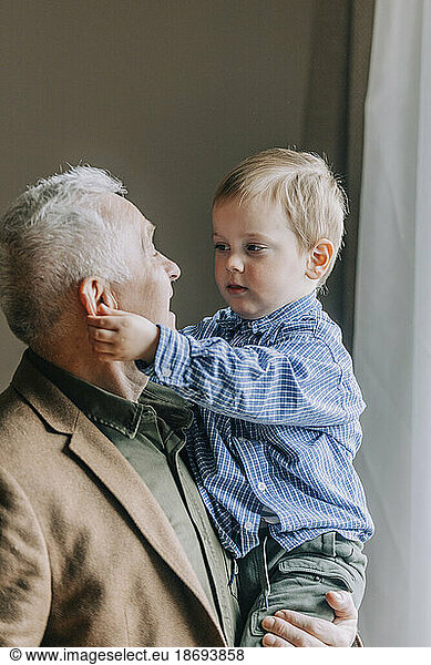 Grandfather carrying grandson at home