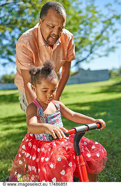 Grandfather pushing granddaughter on tricycle in park