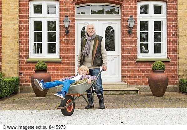 Grandfather pushing grandson in wheelbarrow