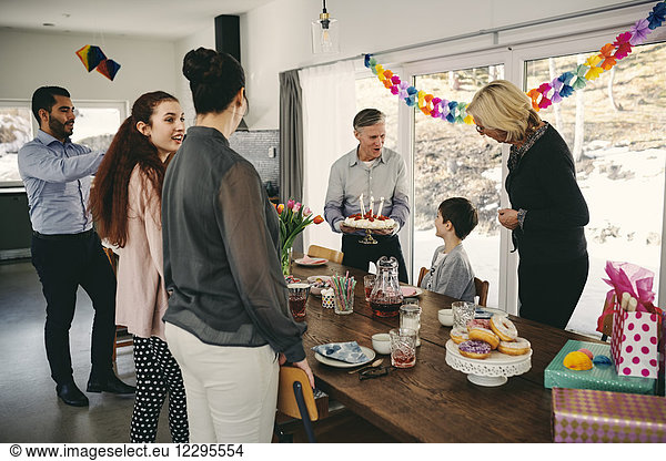 Grandfather showing birthday cake to boy while happy family enjoying at party
