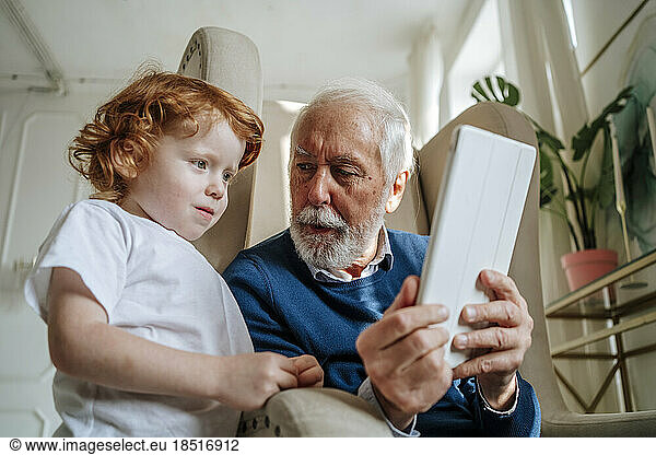 Grandfather showing grandson tablet computer at home
